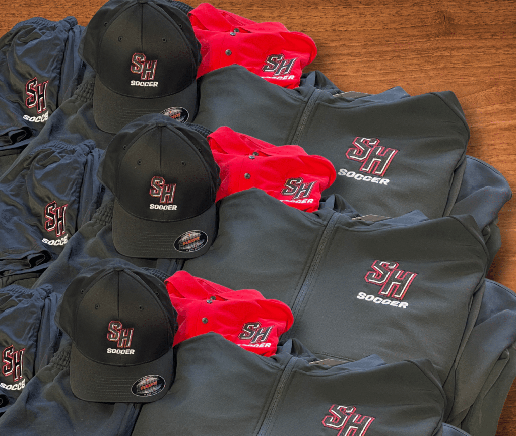 SH Soccer branded black and red apparel including caps, jackets, and shorts.