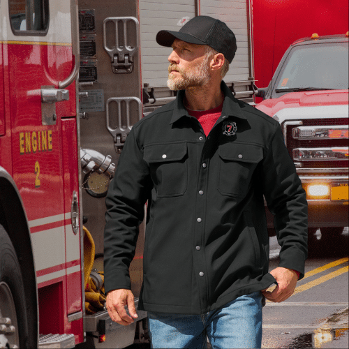 Man wearing a black jacket and cap walking beside a fire engine truck on a city street.