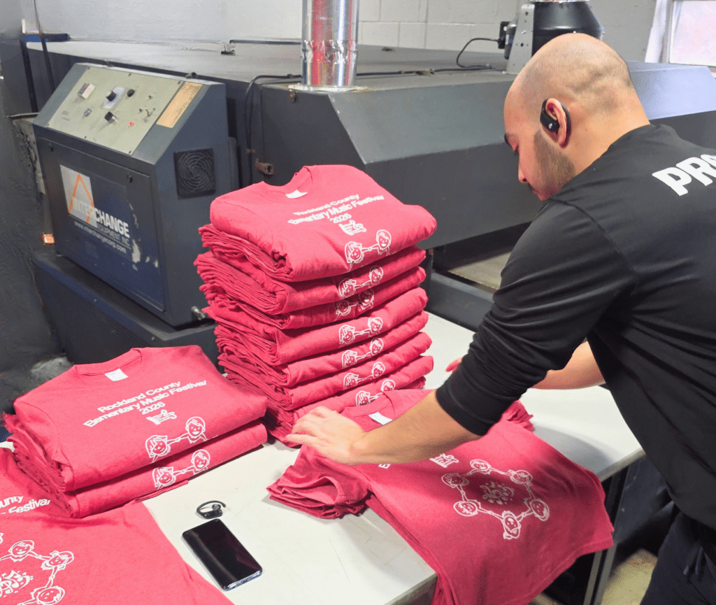 Employee folding red screen-printed event t-shirts in a production facility.