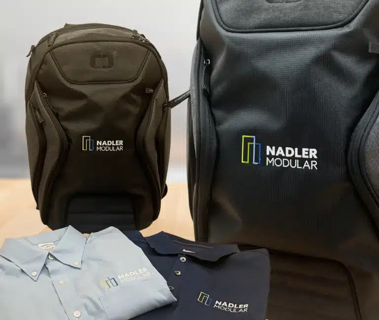 Two Nadler Modular branded backpacks and blue shirts on wooden surface.