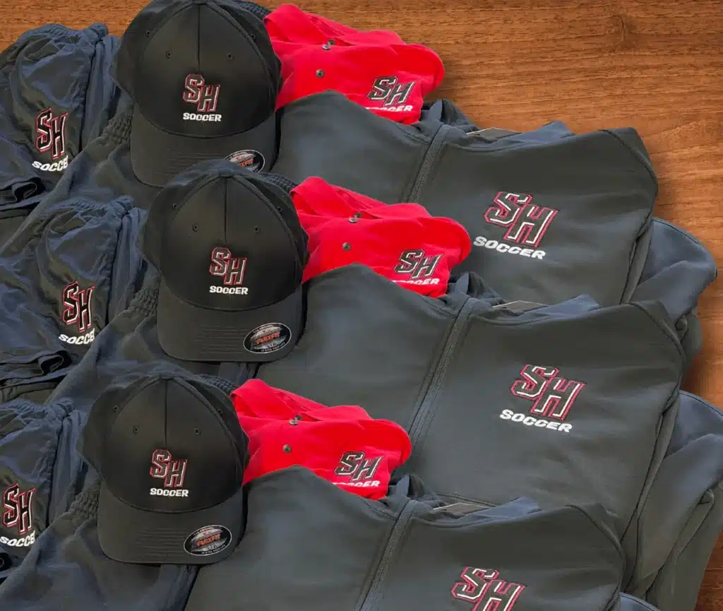 SH Soccer branded black and red apparel including caps, jackets, and shorts.