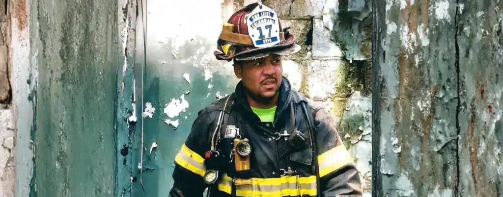 Firefighter in full gear standing inside a burned building with damaged walls, wearing helmet and safety equipment during response operations