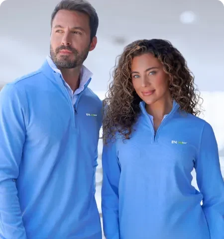 Two professionals wearing matching custom embroidered quarter-zip pullovers, showcasing branded corporate apparel in a clean outdoor setting