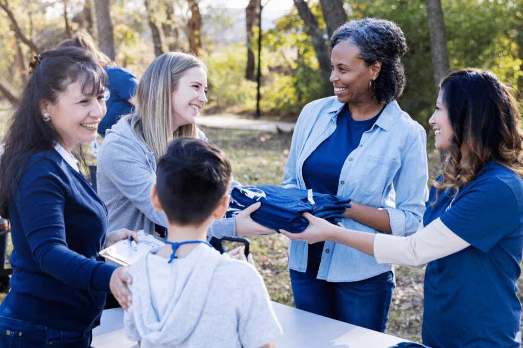 Group of volunteers distributing event t-shirts to attendees at a community gathering.