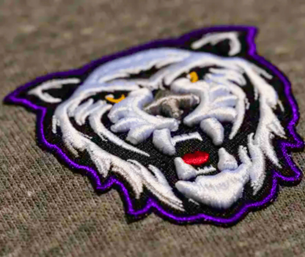 A close up image of embroidered patch of a tiger head, set on a textured fabric background.