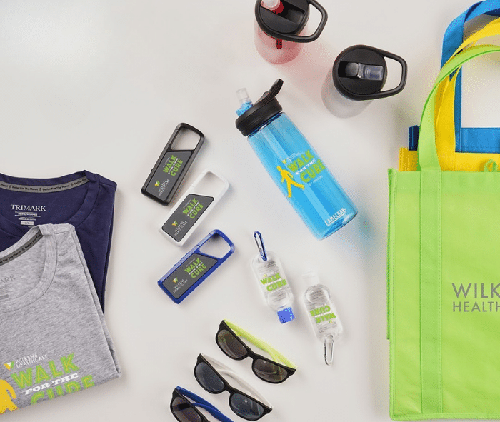 Flat lay of promotional items including t-shirts, water bottles, sunglasses, and a green tote bag.